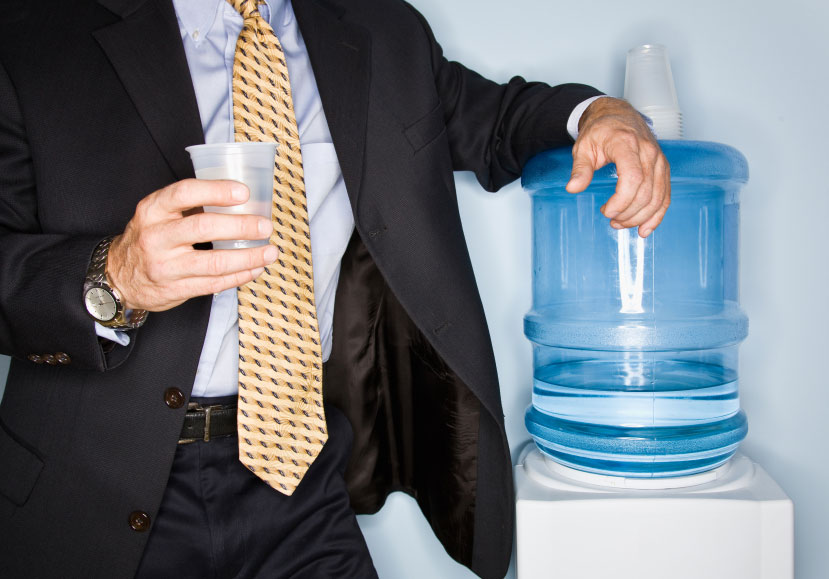A businessman drinking from a water cooler.