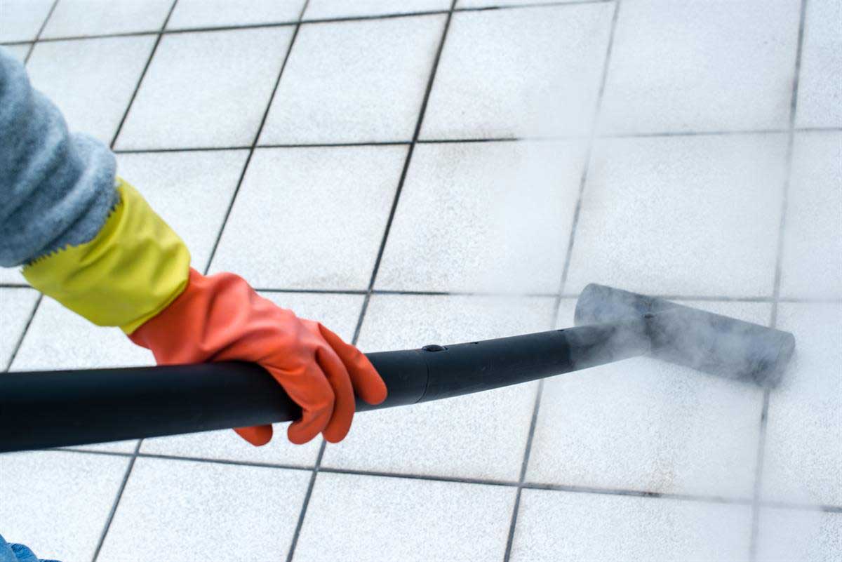 A cleaner using a steam cleaner to clean tile.