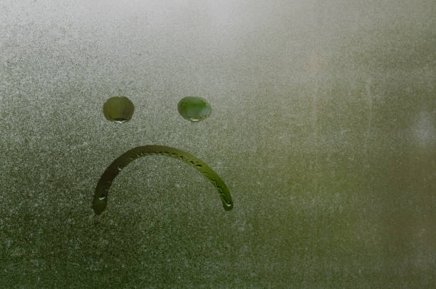 A sad face drawn on the inside of a car windshield.
